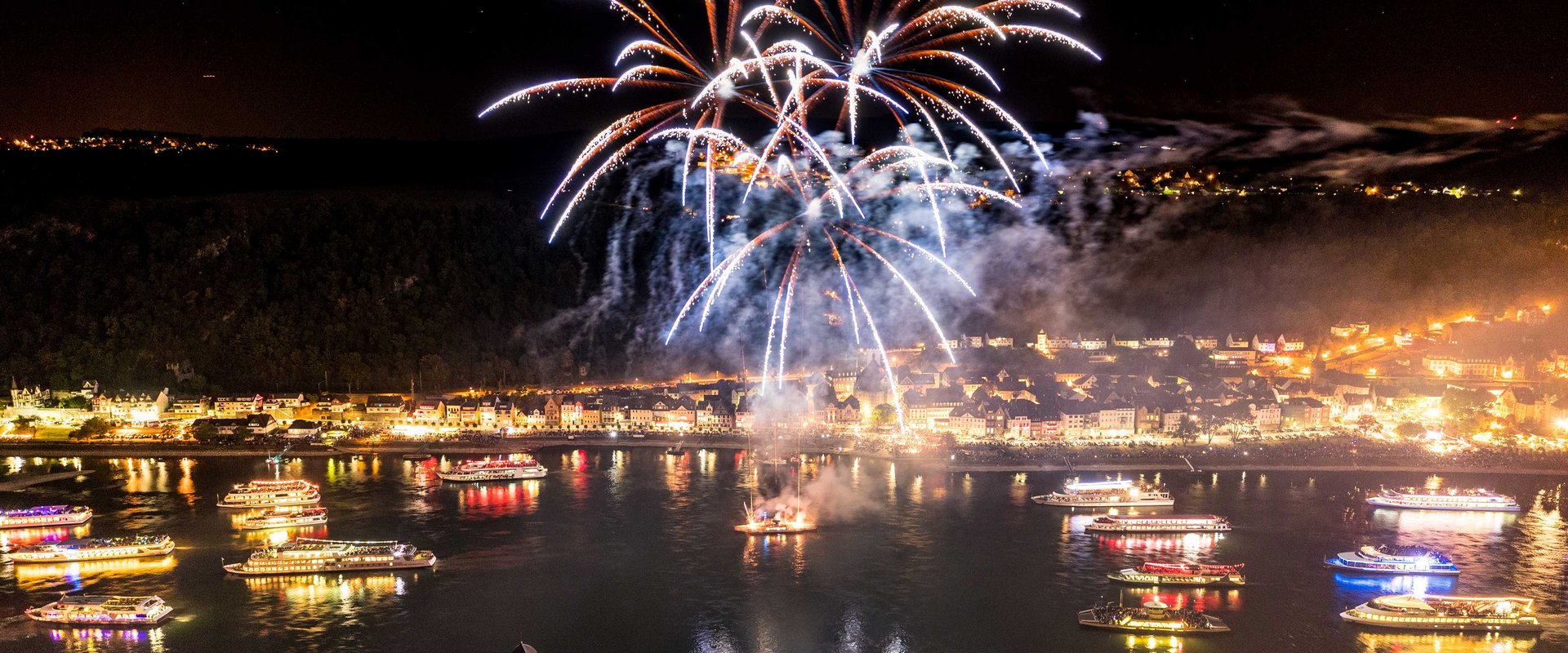 Viele beleuchtete Schiffe auf dem Rhein, Feuerwerk im Hintergrund