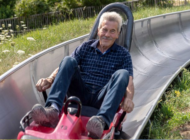 Ein vergnügter älterer Herr rodelt die Sommerrodelbahn herunter
