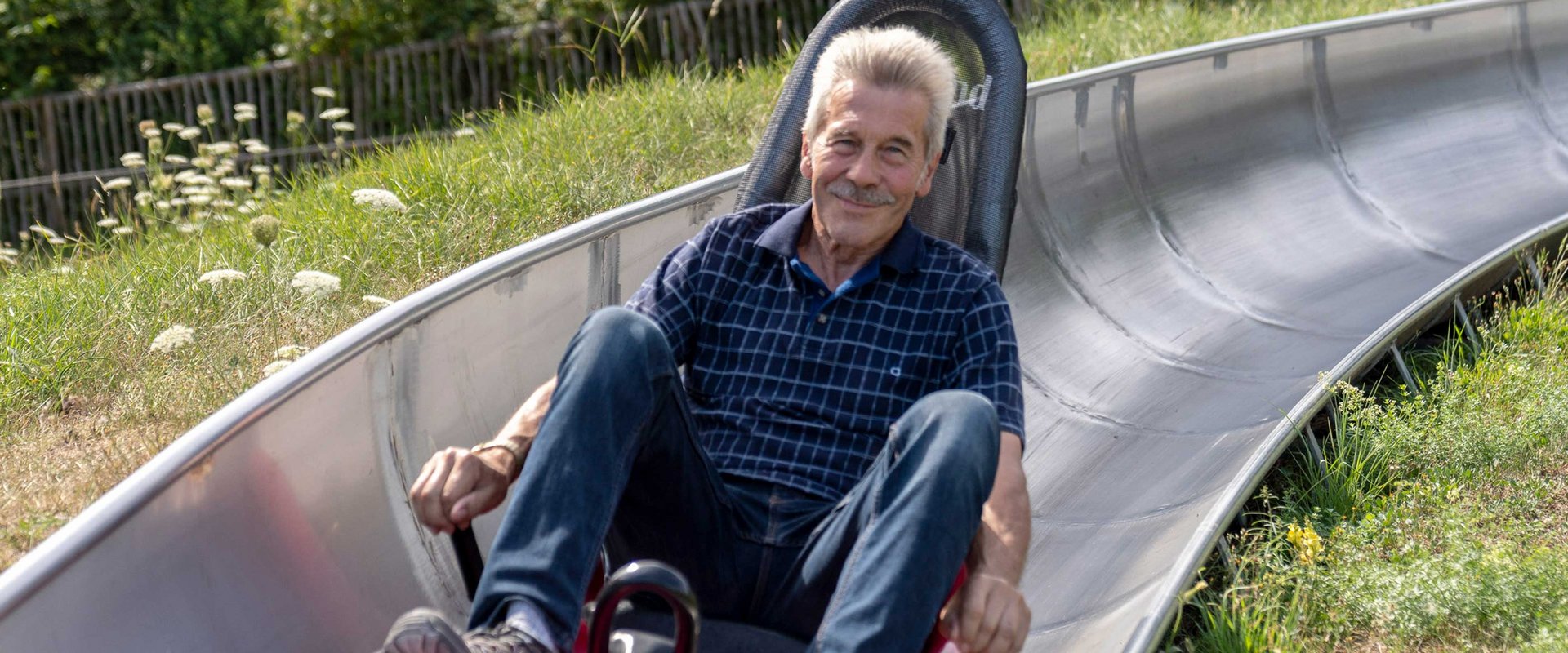 Ein vergnügter älterer Herr rodelt die Sommerrodelbahn herunter