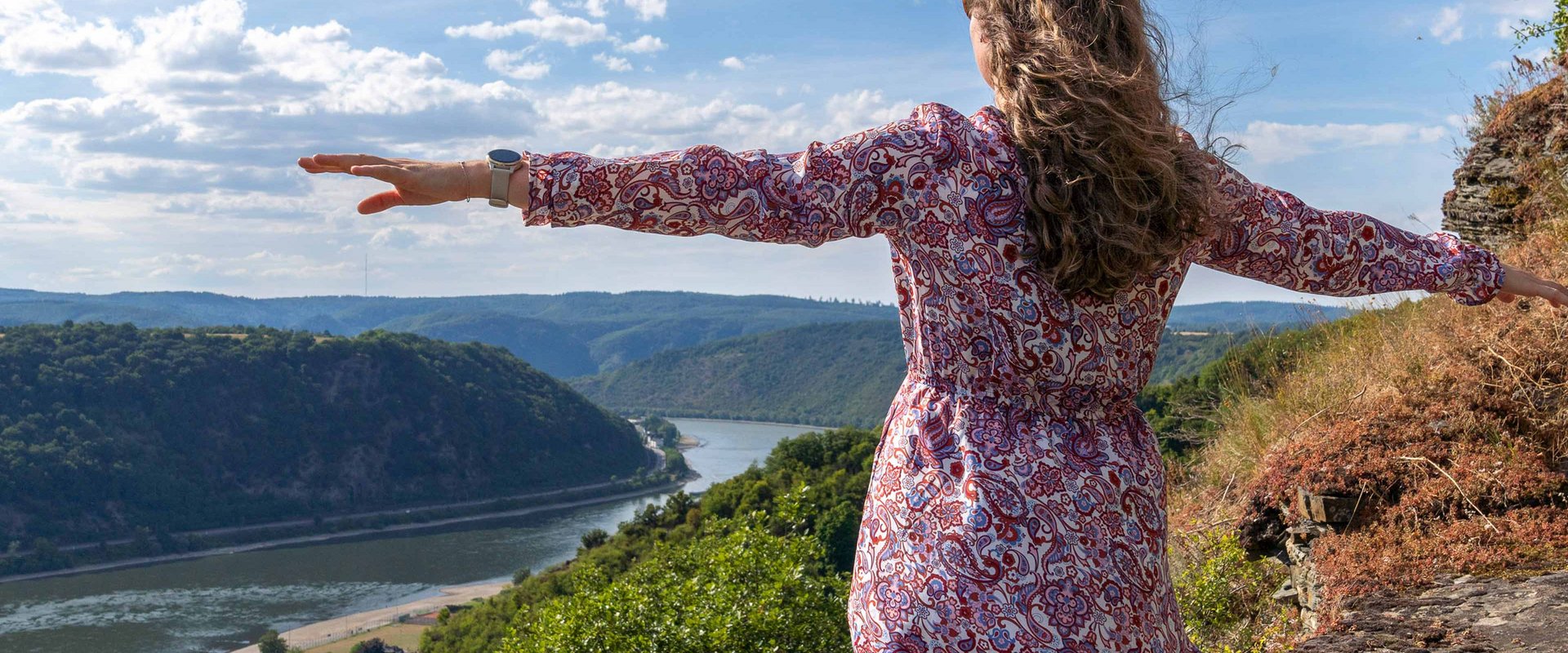 Eine Frau steht auf einem Hügel am Rhein und streckt beide Arme aus