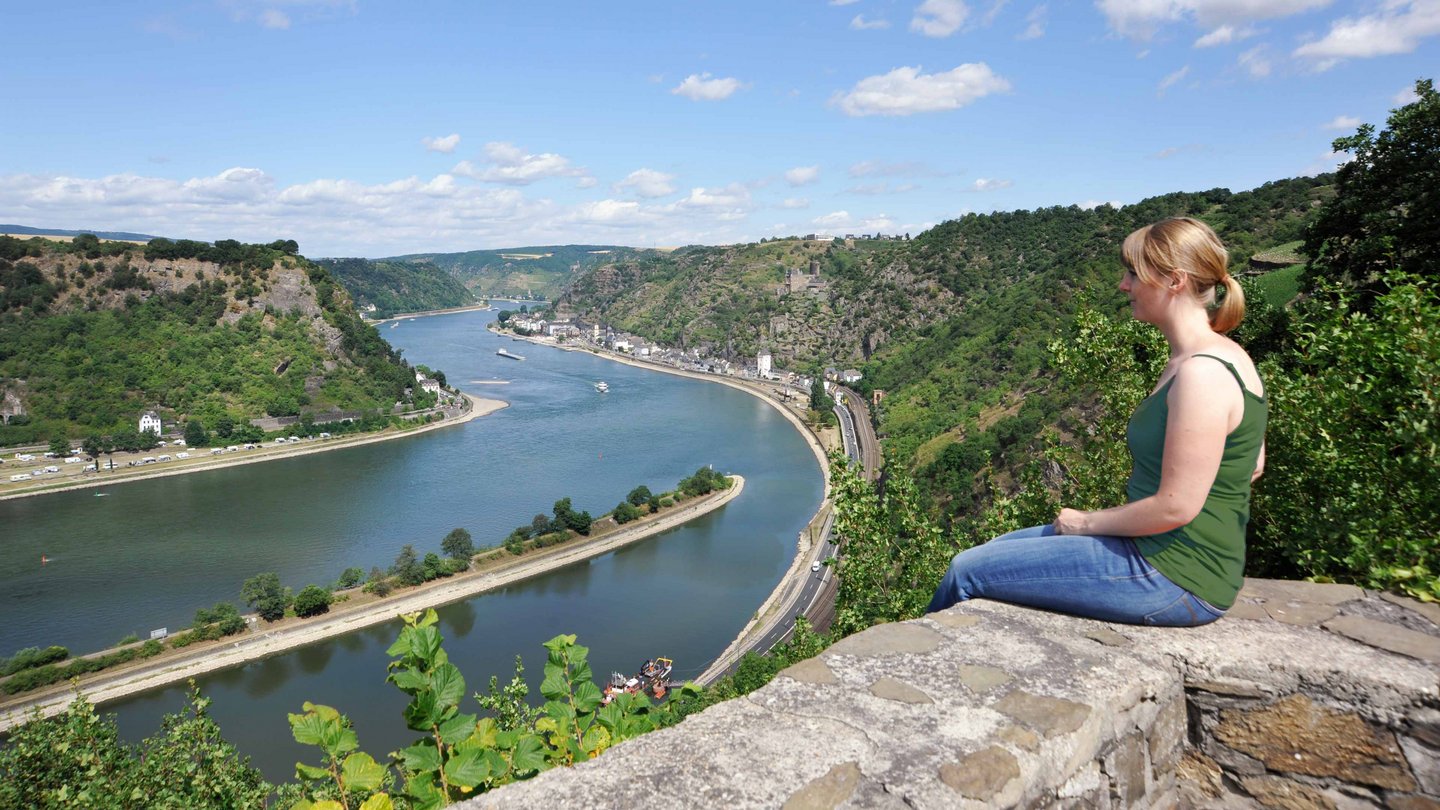 Ein junges Mädchen sitzt auf einem Felsen und schaut auf den Rhein